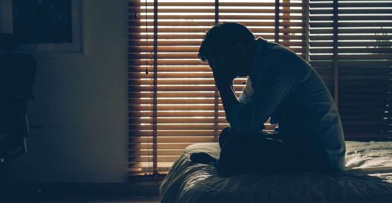 sad-businessman-sitting-head-hands-bed-dark-bedroom